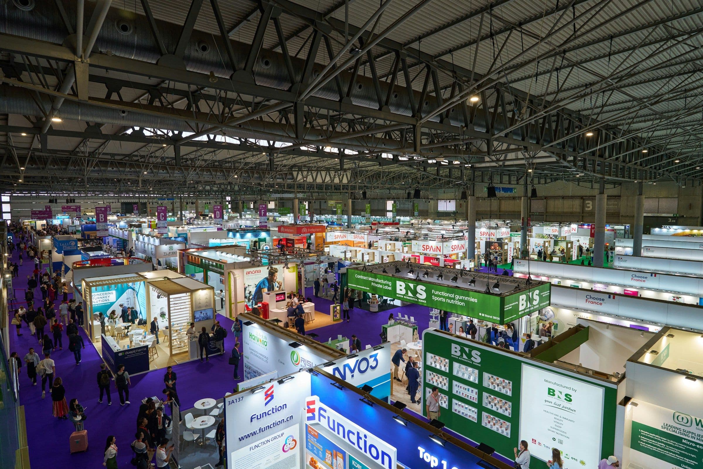 Large trade fair hall with exhibition stands and visitors from above